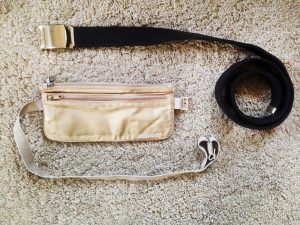 Un marsupio color crema e una cinta nera di stoffa appoggiate su un tappeto bianco a tinta unita